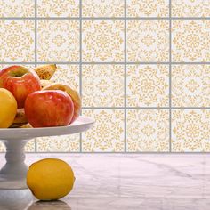 apples and oranges on a white plate in front of a wall with yellow tiles