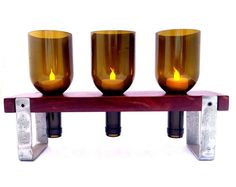 three candles sitting on top of a wooden shelf with metal holders in front of them