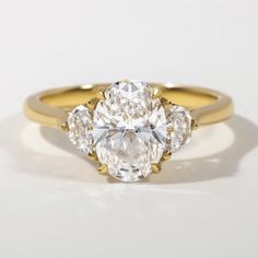 an oval cut diamond ring with three pear shaped diamonds on the band, set in yellow gold