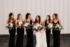 a group of women standing next to each other in front of a white wall holding bouquets