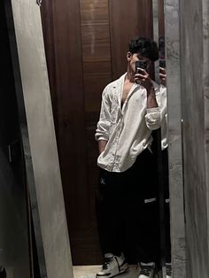 a man taking a selfie in front of a mirror while wearing black pants and white shirt