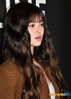 a close up of a person with long hair wearing a brown sweater and white shirt