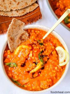 two bowls filled with soup next to some pita bread and a slice of lemon