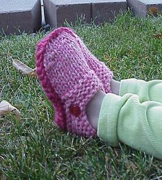 a small child wearing a pink knitted hat laying on the grass next to a sidewalk