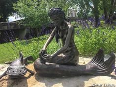 a bronze statue of a woman sitting on top of a rock next to a turtle