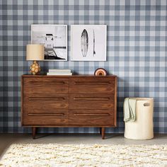 a wooden dresser sitting next to a wall with two pictures on the wall above it