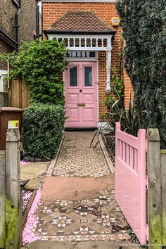 a pink door is in the middle of a brick path leading to a small house