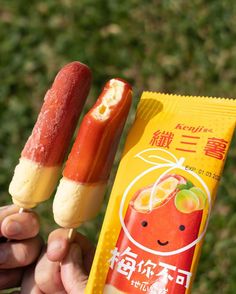 a person holding two popsicles with fruit on them in front of grass and trees