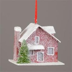 a christmas ornament with a house and trees in the snow, hanging from a red wire