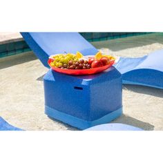 a bowl of fruit sits on top of a blue bench next to a swimming pool