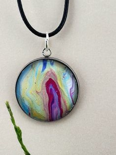 "Looking for a unique and one-of-a-kind gift or a statement piece that will get noticed with any outfit? Our handmade fluid art necklace is a perfect choice! Each necklace is carefully crafted using acrylic pour techniques, creating a unique abstract design that is truly mesmerizing. This necklace would make a unique gift and can be gift-wrapped and shipped directly to the recipient with a card. Shipping is free! I used an acrylic pour technique to create this unique fluid art necklace. Each piece is one-of-a-kind, and no two will ever be alike. This wearable piece of art is protected by a glass cabochon that magnifies the design and gives it a 3D effect. It is set in a hypoallergenic, stainless-steel bezel and hung on a 24\" comfortable, waxed cotton cord. This necklace will look great wi Artistic Pendant Necklace With Artistic Design, Artsy Multicolor Round Pendant Necklace, Artsy Multicolor Round Pendant Jewelry, Multicolor Artistic Pendant Necklace, Artsy Multicolor Jewelry With Large Pendant, Artsy Multicolor Necklaces With Artistic Design, Artistic Round Pendant Necklace, Wearable Art Necklace With Large Pendant, Artistic Necklace With Round Pendant