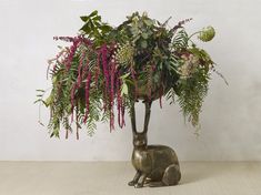 a vase filled with lots of flowers and greenery next to a rabbit figurine