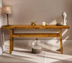 a wooden table with candles on it next to a vase and candle holder in the corner