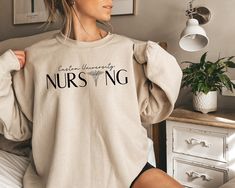 a woman sitting on top of a bed wearing a white shirt with the words nursing printed on it