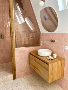 a bathroom with pink tiles and a wooden sink counter in front of a round mirror