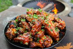 chicken wings covered in bbq sauce on a plate next to an open fire pit