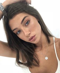 a close up of a person wearing a white tank top and holding her hand on her head