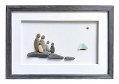 an art work with rocks and a small boat in the water, on display inside a white frame