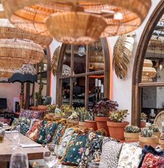 a restaurant with lots of tables and chairs covered in cushions, potted plants and wicker hanging from the ceiling