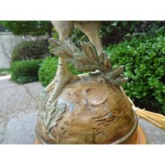 a statue of a bird on top of a potted plant in front of some bushes