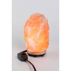 an orange himalayan salt lamp sitting on top of a wooden stand next to a black cord