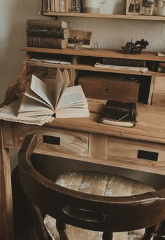 an open book on top of a wooden desk next to a chair and bookshelf