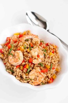 a white bowl filled with rice and shrimp on top of a table next to a fork