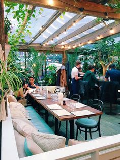 people sitting at tables in a restaurant with plants growing on the walls and wooden beams