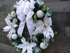 a wreath with white and green decorations hanging on a wooden wall next to a fence