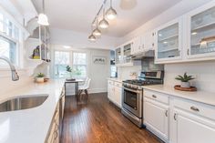 a kitchen with white cabinets and wood floors is pictured in this image, there are lights hanging from the ceiling over the stove