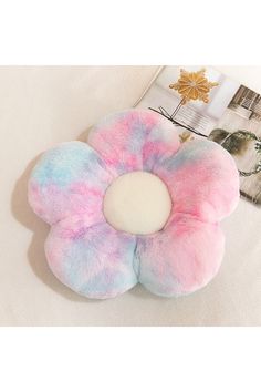 a pink and blue flower shaped pillow sitting on top of a white bed next to a magazine