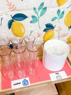 several glasses are lined up on a table next to a bucket with ice and lemons