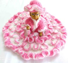 a pink and white crocheted doll sitting on top of a round object with gold eyes