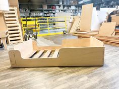 a wooden bed frame sitting on top of a hard wood floor next to stacks of lumber