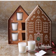 a gingerbread house shaped candle holder with three candles in front of it next to two glasses