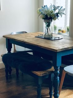 a wooden table sitting in front of a window next to a chair and vase with flowers