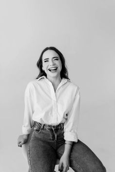 a woman sitting on top of a stool smiling at the camera with her hands in her pockets