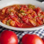 some tomatoes are in a white bowl on a checkered table cloth