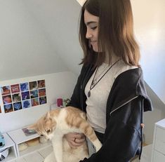 a woman holding an orange and white cat in her arms while standing next to a desk