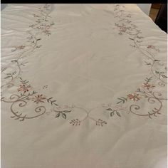 an embroidered tablecloth with flowers and vines on it, sitting on top of a bed