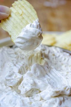 a hand holding a cracker over a bowl of white dip with chips on the side