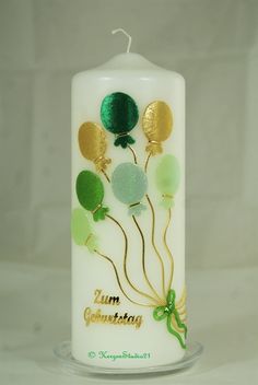 a white candle with green and gold balloons on it