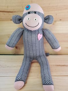 a sock monkey with a pink heart on it's chest sitting on a wooden floor