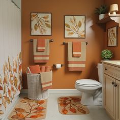 a bathroom with orange walls and towels hanging on the rack above the toilet, along with rugs