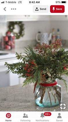 a glass jar filled with red berries and greenery on top of a kitchen counter