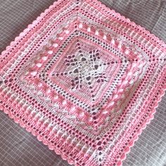 a pink crocheted square sitting on top of a bed next to a pillow