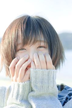 a woman covering her face with both hands and looking at the camera while standing in front of water