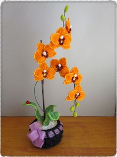 a crocheted plant with orange flowers in a black pot on a wooden table