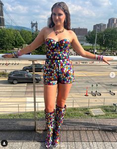 a woman standing on top of a sidewalk next to a fence and wearing colorful boots