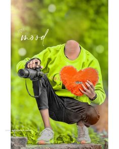 a young man holding a heart shaped pillow in front of his face while sitting on a rock